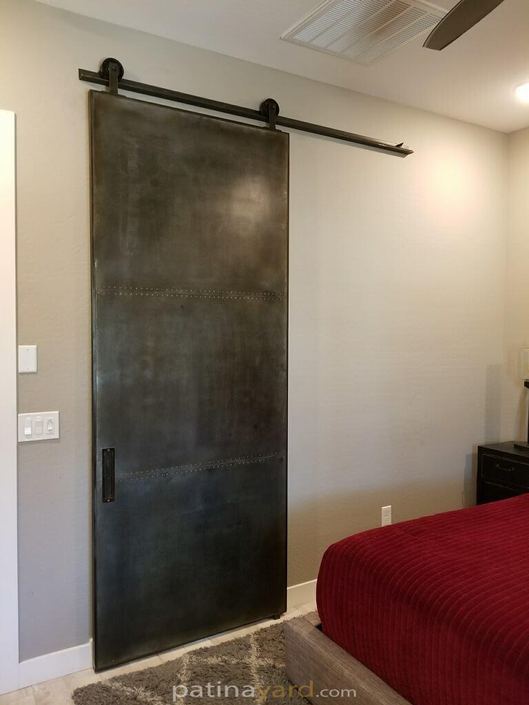 Steel panel barn door with rivets in the seams and patina finish